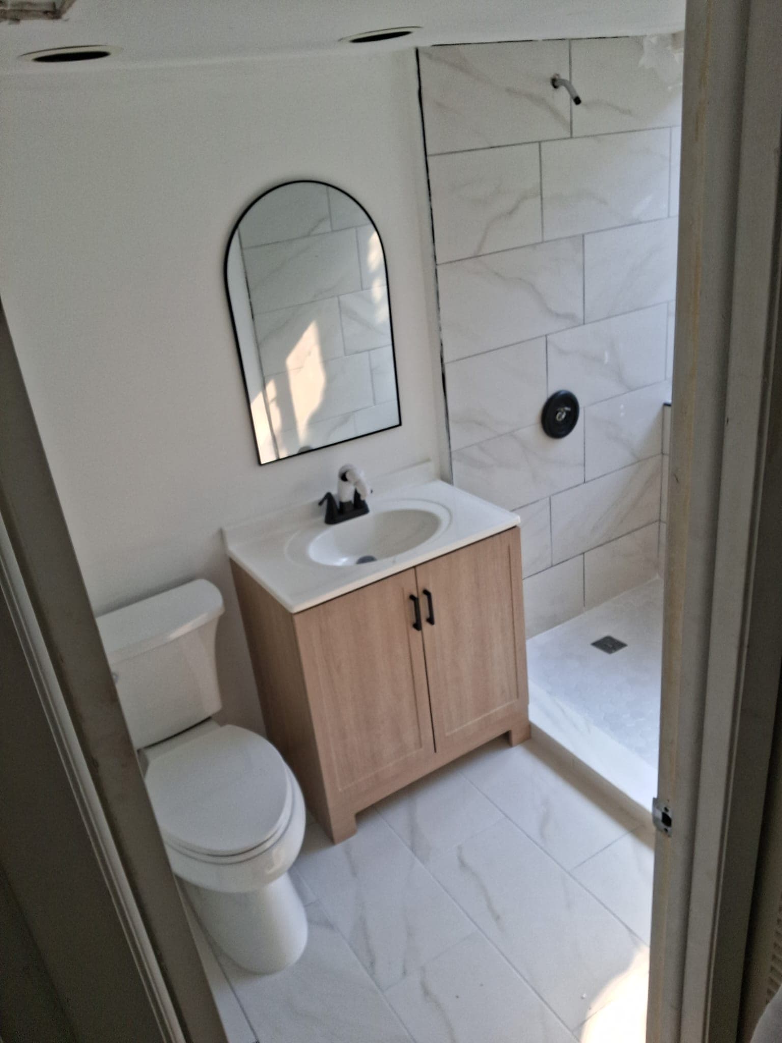 Finished bathroom remodel with a light wood vanity and white tile shower.